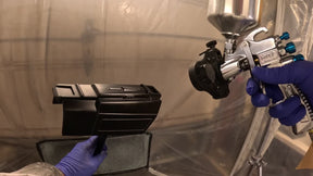Spray gun beside a gloss-black forearm armor part in the workshop booth